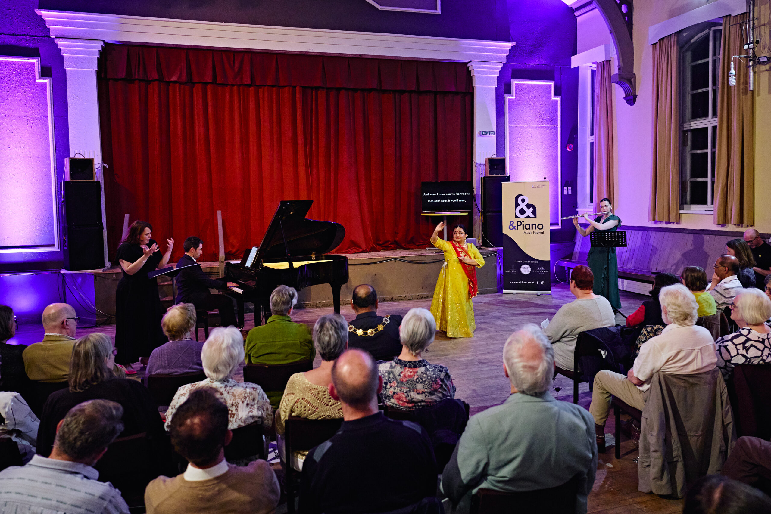 An indian dancer dancing to an audience with a flute and piano and singer.
